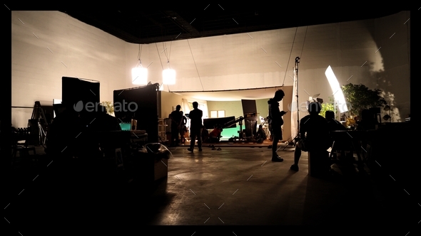 Silhoutte images of video manufacturing and lighting established for filming which film crew group working and