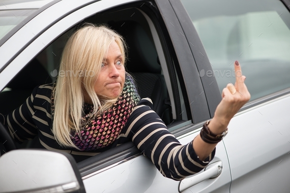 Angry mature blonde woman driving and flipping people off with middle finger,expressing emotion